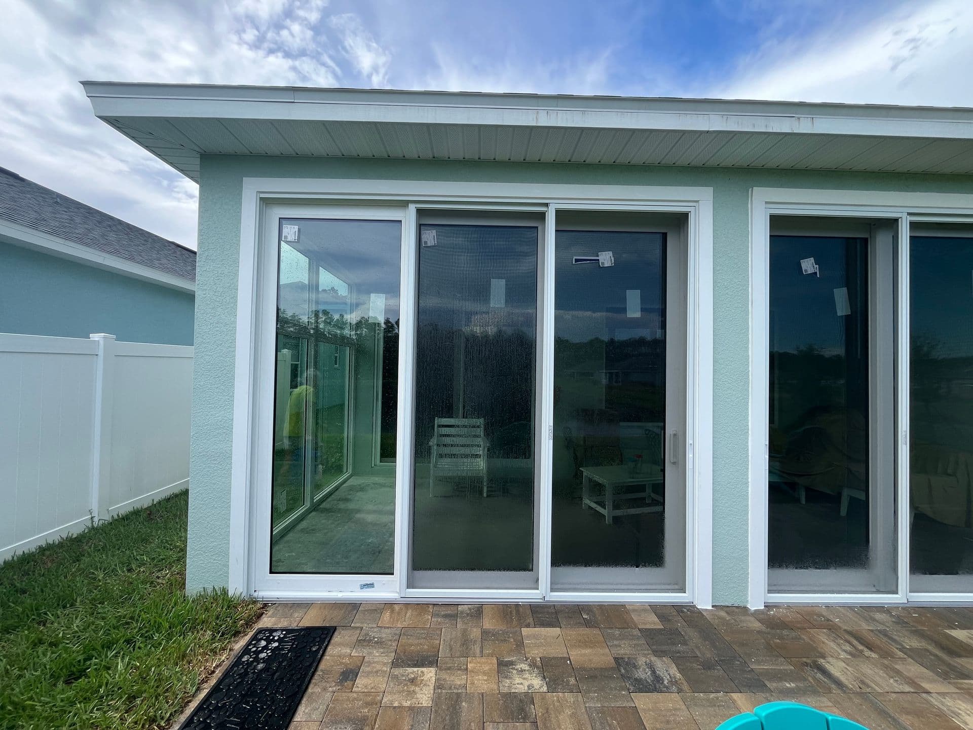 Modern home exterior with multiple white-framed sliding glass doors opening to a patio, featuring a turquoise textured wall and metal roof overhang